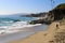 Vast blue ocean water crashing into the rocks along the beach with homes along the coastline with lush green palm trees