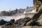 Vast blue ocean water crashing into the rocks along the beach with homes along the coastline with lush green palm trees