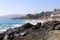 Vast blue ocean water crashing into the rocks along the beach with homes along the coastline with lush green palm trees