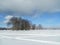 Vast countryside expanse, covered by abundant snow blanket under cloudy blue sky.