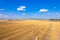 Vast expanse of rolling hills dotted with round bales of hay against a clear, brilliant blue sky