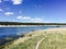 Vast lake surrounded by lush verdant grass and trees illuminated by the bright blue sky