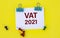 VAT 2021 - acronym on white paper with clips on yellow background with buttons and pencil