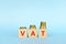 VAT letters on wooden blocks in blue background increasing stack of coins. Increase on value added tax