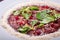 Veal carpaccio on a white plate with grated parmesan cheese with basil