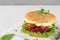 Vegan beetroot burger with avocado, salad, tomato, sprouts and vegan mayonnaise on white marble table