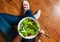 Vegan breakfast meal in bowl with various fresh mix salad leaves and tomato. Girl in jeans holding fork with knees and hands visib