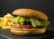 Vegan burger with seitan cutlet and french fries on black slate plate in low key