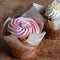 Vegan cupcakes surrounded in parchment paper, with piped cream on top, served on a rustic olive wood platter.