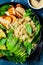 Vegan lunch plate. Quinoa salad with baked zucchini, sweet potato, avocado and tahini dressing in black plate, dark background,