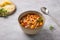 Vegan seasonal italian minestrone soup with pumpkin, beans, tomatoes, bell peppers, pasta and herbs on gray textured background