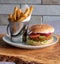 Vegan soya burger with french fries served in a small metal bucket with napkin, served on an olive wood platter.