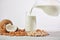 Vegetable milk is poured into a glass from a jug on a wooden background.