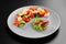 Vegetable salad of tomatoes cucumbers mushrooms and fetta cheese on grey plate on black background isolated