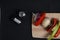 Vegetable shashlick on spitter on cutting board and salt and pepper shaker on black background flat lay