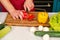 Vegetables getting cut on wooden cutting board. Hand slice pepper with ceramic knife. Food preparation and cooking