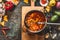 Vegetarian Bean soup in cooking pot with ladle on wooden cutting board with ingredients on dark rustic background, top view, frame