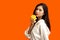 Vegetarian concept, Healthy woman eating yellow bell pepper standing in isolated orange background