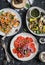 Vegetarian dinner table - quinoa and pumpkin salad, tomatoes, eggplants and peppers on the grill. On a dark background, top view.