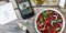 Vegetarian lunch. Salad of fresh vegetables, greens and red sweet peppers with olive oil. On the smartphone screen, a