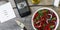 Vegetarian lunch. Salad of fresh vegetables, greens and red sweet peppers with olive oil. On the smartphone screen, a