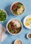 Vegetarian lunch table in the asian style - rice, noodles, vegetable stir fry, boiled eggs. On a blue background