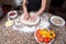 Vegetarian Pizza Preparation - Baker Kneading Dough Surrounded By Ingredients On Marble Table In The Kitchen