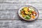 Vegetarian salad of pac choi cabbage, kiwi, tomatoes, kumquat, microgreen sprouts on gray wooden background. Side view, copy space