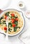 Vegetarian whole grain spaghetti pasta with cherry tomatoes and spinach sauce in a cast iron pan on a white background, top view.