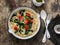 Vegetarian whole grain spaghetti pasta with cherry tomatoes and spinach sauce in a cast iron pan on a wooden background, top view.