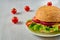 Veggie burger with salad, onion rings and cheese decorated with fresh cherry tomatoes on the gray concrete background