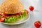 Veggie burger with salad, onion rings decorated with fresh cherry tomatoes on the gray concrete background with free copy space