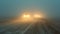 Vehicles cautiously navigating a road during a dust storm, with headlights barely piercing through the thick dust