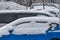 Vehicles covered in snow in a parking lot during a winter snowfall