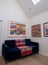 Velvet blue sofa with colourful wool blanket throw, in minimalist setting with white walls and colourful artwork.