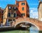 Venetian canal between old buildings and small brick footbridge on foreground, Italy.