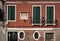 Venetian red facade of old house with religious scene, green windows and typical oval windows. Venice, Italy