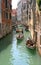 VENICE, ITALY - AUGUST 22, 2008: Gondoliers with passenger tourists float on gondolas along a narrow channel under bridge