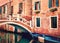 Venice, Italy. Small bridge over canal with blue boat and traditional orange historic buildings.