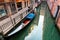 Venice on a peaceful morning, with view of an elegant gondola parking on a narrow canal, a tourist sitting by the quiet alley