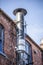 Ventilation tube chimney on the red brick house. Blue sky in the background. Metal chimney on the old brick house.