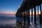 Ventura Pier at Sunset. Beach with rocks in foreground, smooth ocean; colored sky in background.