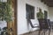 Veranda with chairs and table on the wooden floor. Front facade with door and windows and plants