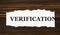 VERIFICATION - word on a white tattered piece of paper on a wooden background