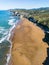 Vertical aerial of foamy turquoise waves hitting the shore of Playa de Sopelana beach in Spain