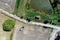 Vertical aerial view over a path next to a harvested field and a meadow with a small stable in front of a pond for fishing