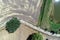 Vertical aerial view over a path next to a harvested field and a meadow with a small stable near a narrow moat.