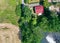 Vertical aerial view of a small hut with a red saddle roof on a country road with bushes and trees and a field and meadows in the