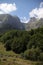 Vertical of Aran valley with forested, misty, sunlit Pyrenees mountain range, cloudy sky background