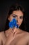 Vertical attractive woman with blue make up and flower near face look at camera on black background. Fragrance cosmetic